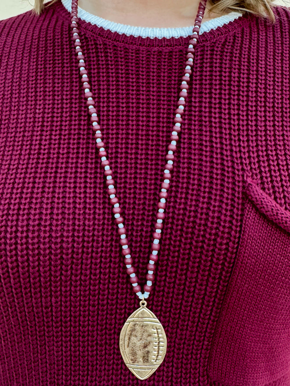 Long beaded necklace with alternating garnet and white beads, featuring a gold football pendant. A bold yet fun Gameday accessory.
