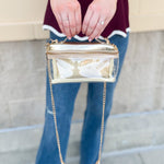 Clear stadium-approved bag with gold vegan leather accents, gold chain strap, and zipper.