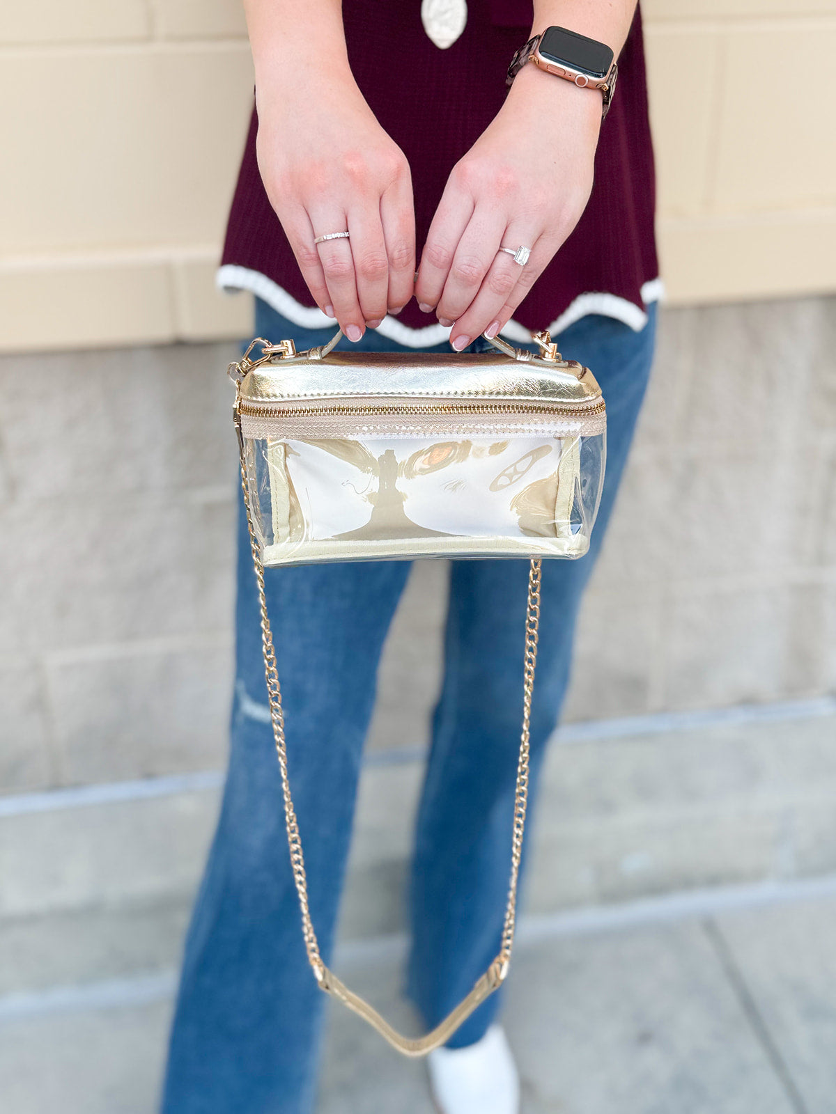 Clear stadium-approved bag with gold vegan leather accents, gold chain strap, and zipper.