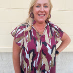 Satin blouse with ruffle collar, v-neckline, flare raglan sleeves, and abstract garnet, gold, black, and white print.
