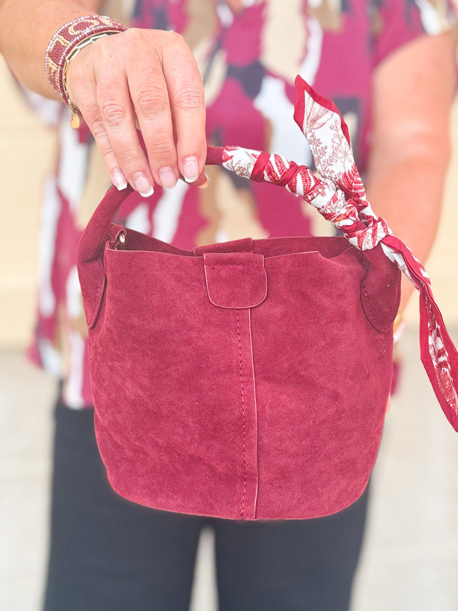 Small garnet faux suede bucket bag with cream-and-garnet patterned scarf accent and crossbody strap.