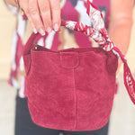 Small garnet faux suede bucket bag with cream-and-garnet patterned scarf accent and crossbody strap.