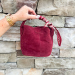 Small garnet faux suede bucket bag with cream-and-garnet patterned scarf accent and crossbody strap.