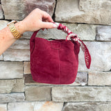 Small garnet faux suede bucket bag with cream-and-garnet patterned scarf accent and crossbody strap.