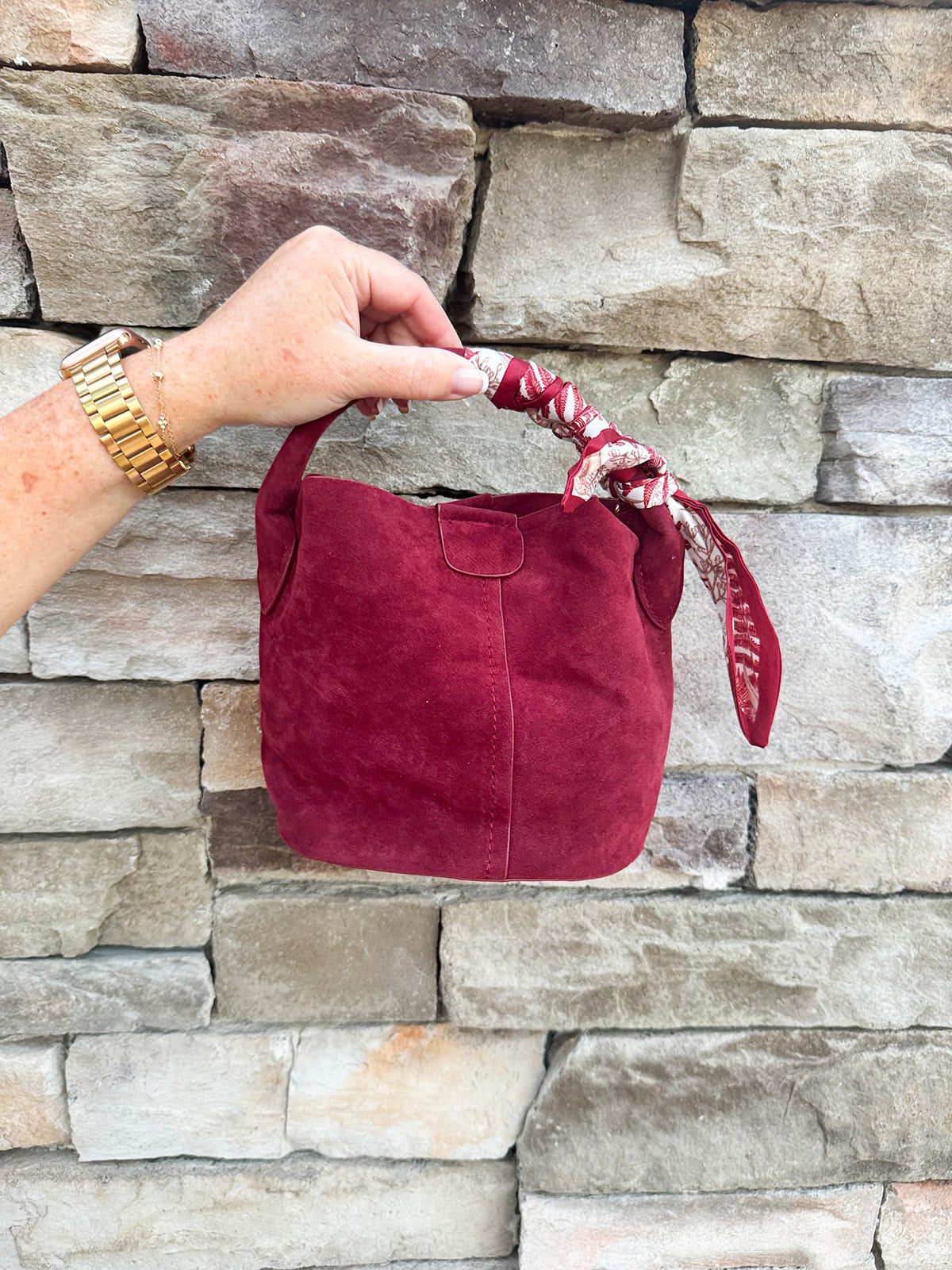 Small garnet faux suede bucket bag with cream-and-garnet patterned scarf accent and crossbody strap.