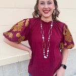 Garnet short sleeve blouse with ruffle neckline and puff sleeves featuring gold/caramel velvet floral appliqué.