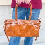 Structured caramel brown glossy faux leather tote with rounded handles and buckle accents.