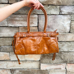 Structured caramel brown glossy faux leather tote with rounded handles and buckle accents.