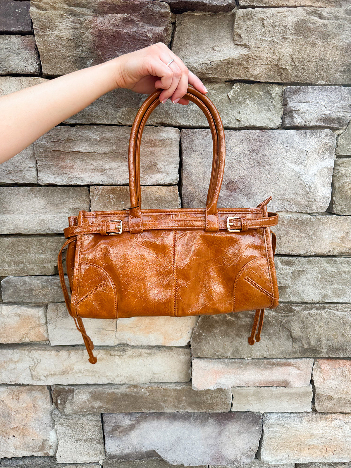 Structured caramel brown glossy faux leather tote with rounded handles and buckle accents.