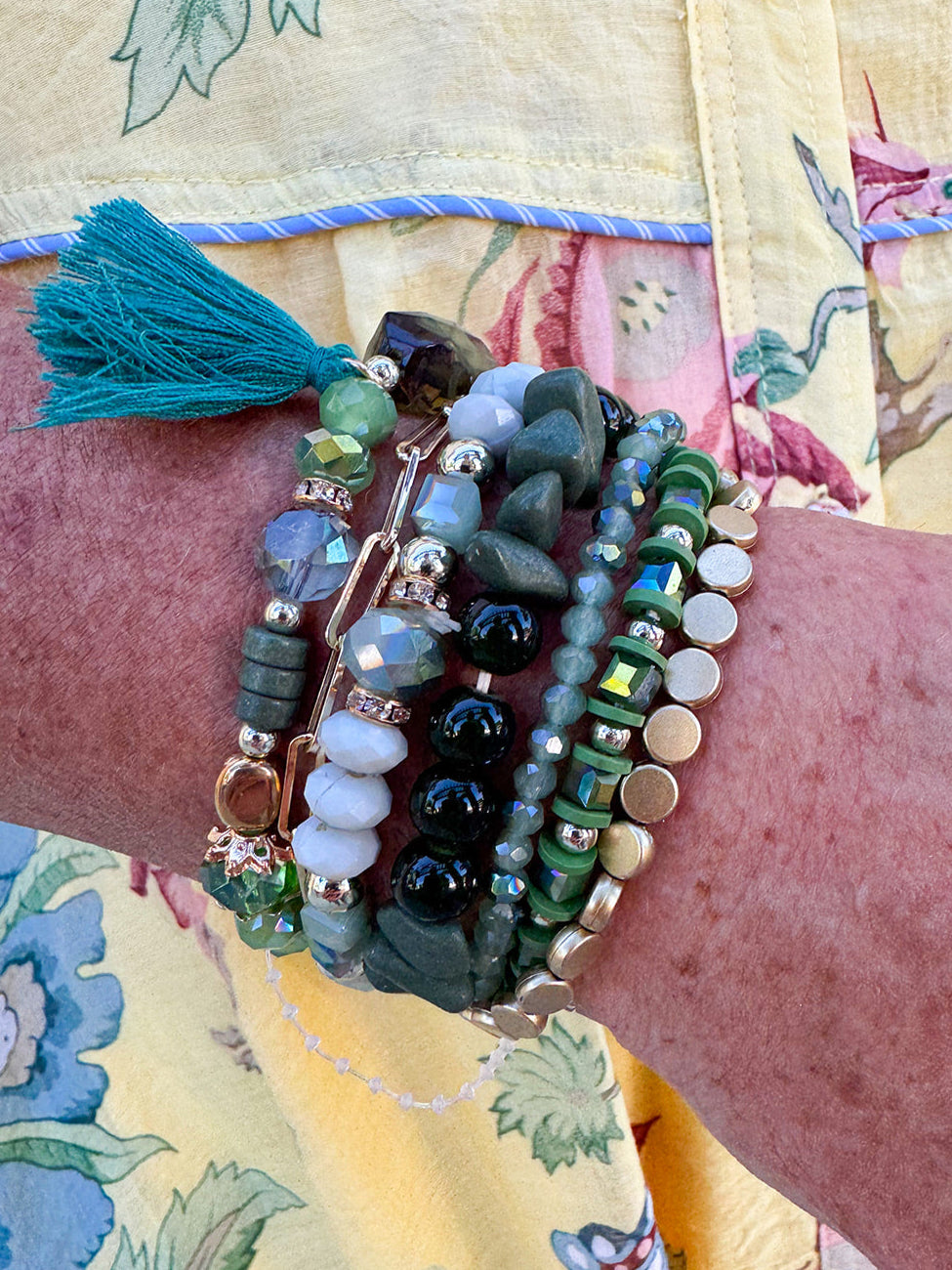 Green multi-strand tassel bracelet with assorted beads and charms, stretchable for easy wear.
