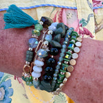 Green multi-strand tassel bracelet with assorted beads and charms, stretchable for easy wear.