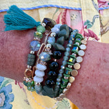 Green multi-strand tassel bracelet with assorted beads and charms, stretchable for easy wear.