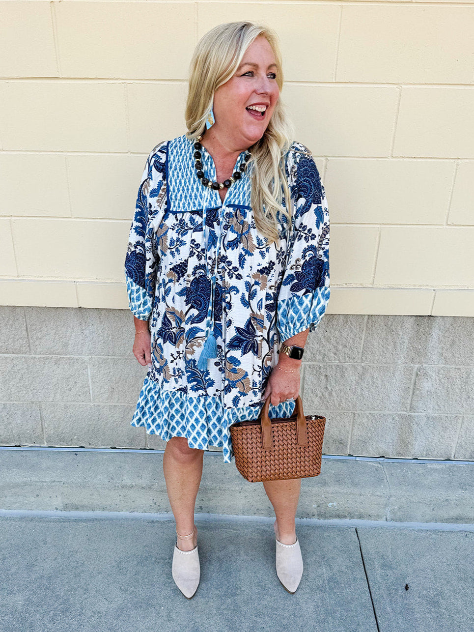 Mini dress with paisley-inspired print in soft blue, light orange, and cream, featuring tassel tie neckline and ¾ sleeves.