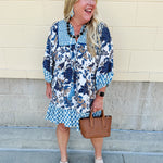 Mini dress with paisley-inspired print in soft blue, light orange, and cream, featuring tassel tie neckline and ¾ sleeves.