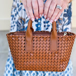 Person holding a woven brown handbag with a blurred background