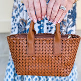Person holding a woven brown handbag with a blurred background