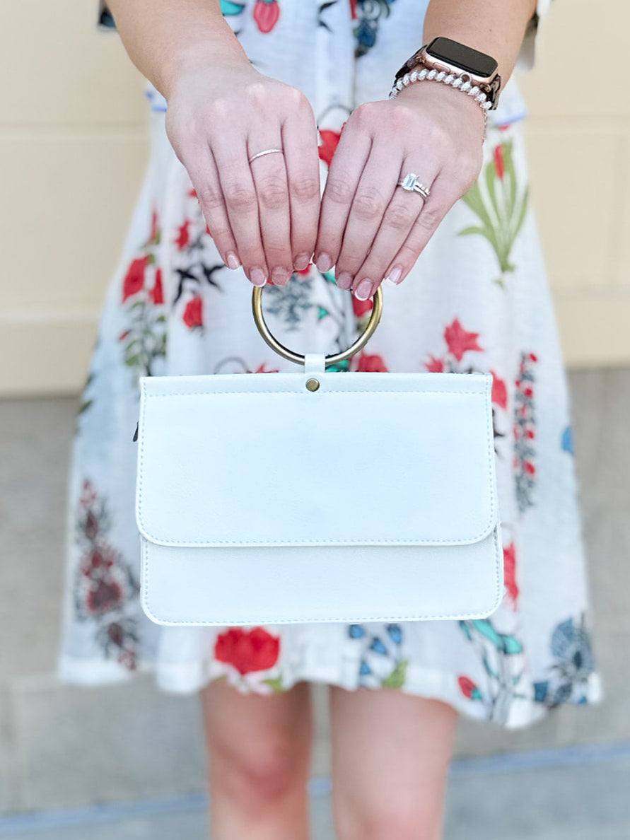 Joy Susan Aria Ring Bag in White displayed with a metallic ring handle, crisp vegan leather finish, and compact silhouette – styled as a wristlet, clutch, or crossbody for a versatile day-to-night look