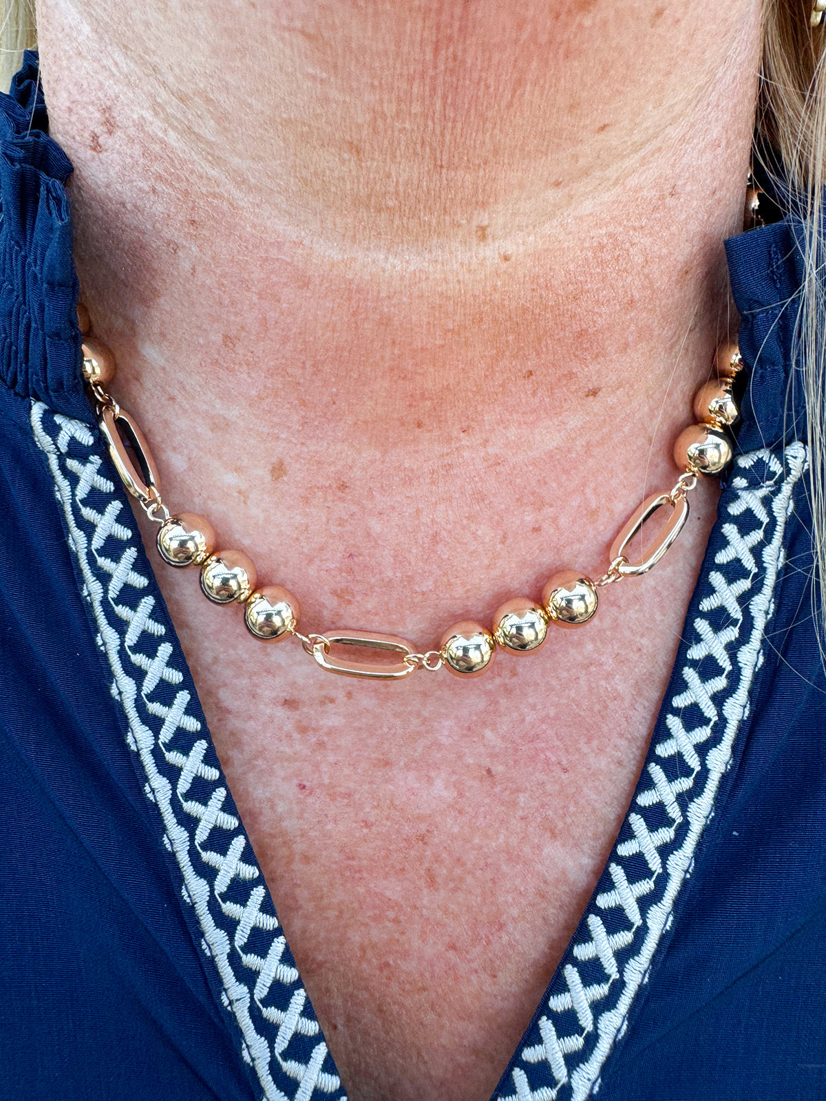 Gold beaded necklace with alternating round beads and open oval beads, adjustable length.