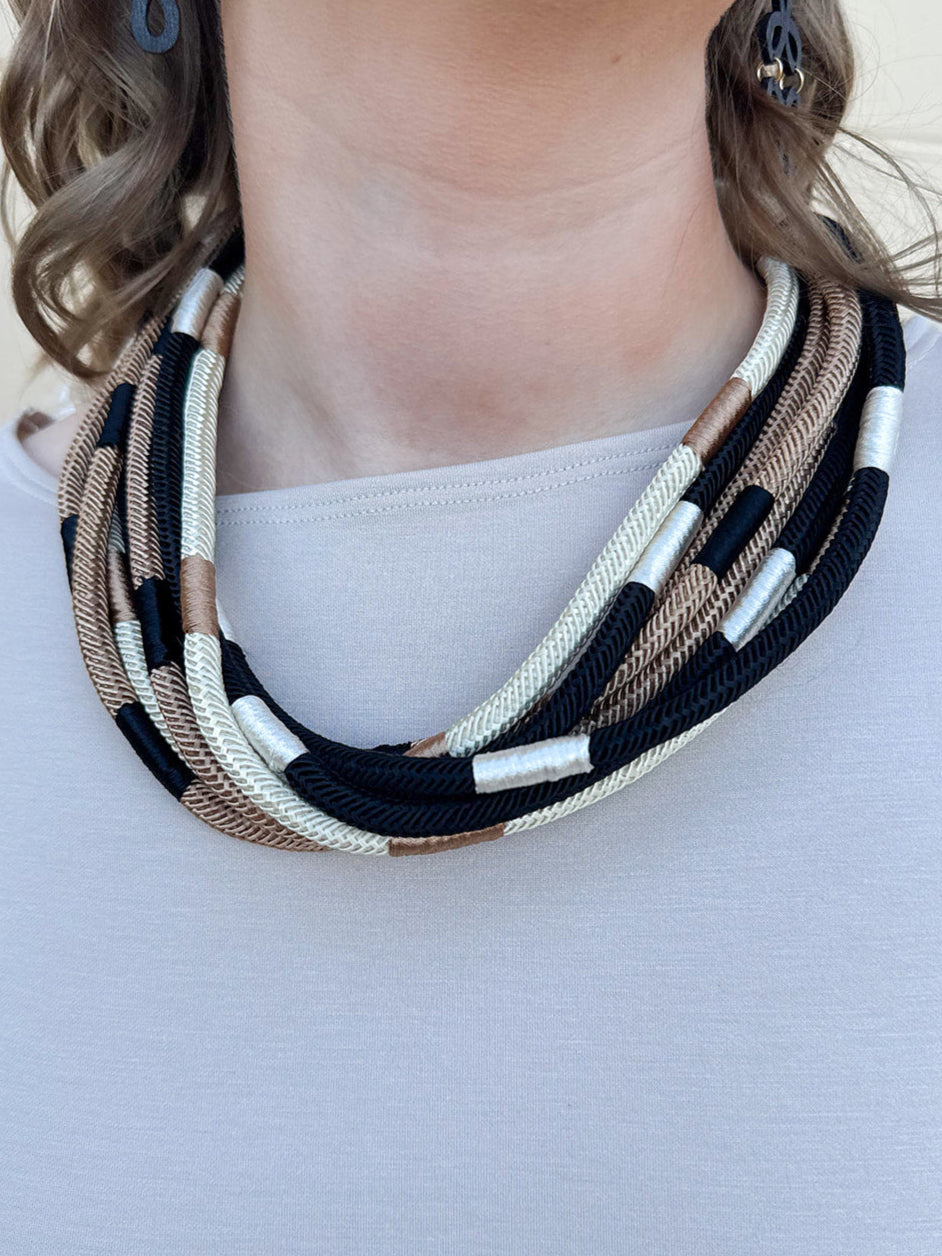 Multi-strand rope necklace in cream, khaki, and black with color-blocking details and ball-and-eye closure.