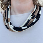 Multi-strand rope necklace in cream, khaki, and black with color-blocking details and ball-and-eye closure.