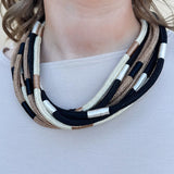 Multi-strand rope necklace in cream, khaki, and black with color-blocking details and ball-and-eye closure.
