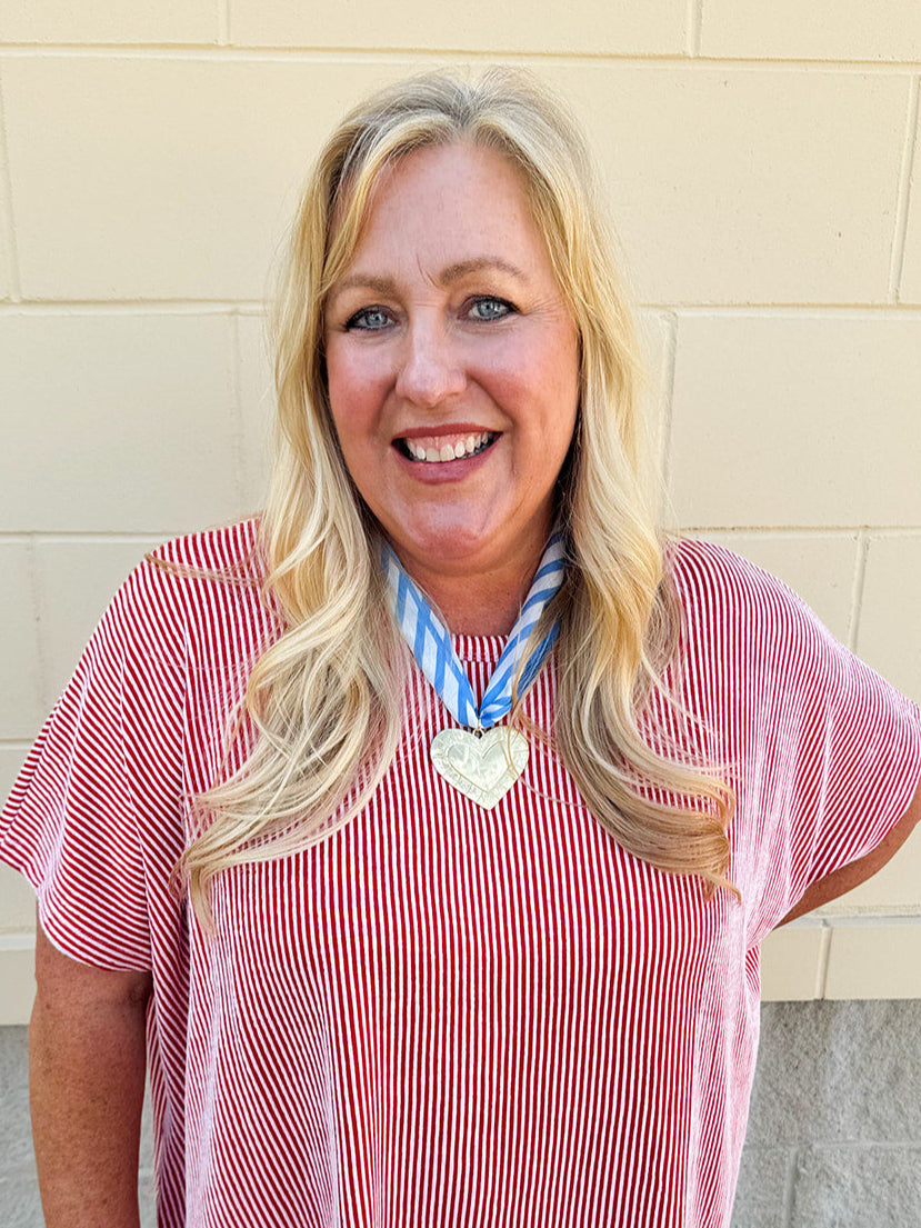 Light blue and white striped fabric scarf necklace with a gold heart charm and a tied back, styled as a feminine accessory.