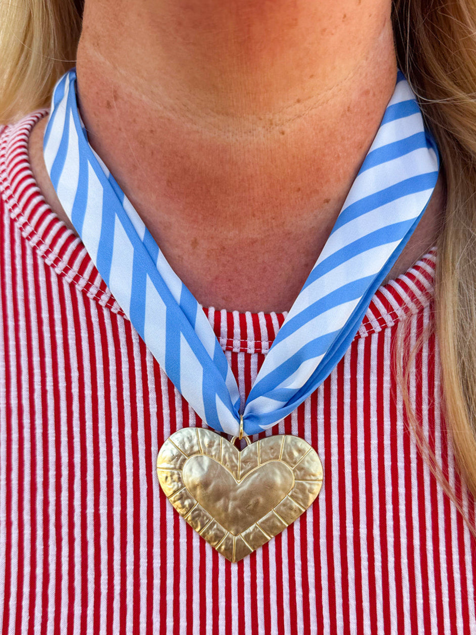 Light blue and white striped fabric scarf necklace with a gold heart charm and a tied back, styled as a feminine accessory.