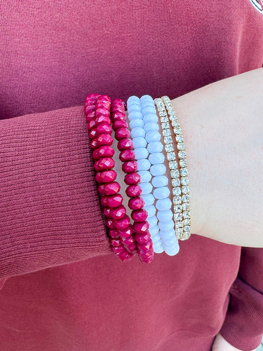 A seven-piece bracelet stack with white, diamond-style, and garnet beaded bracelets, styled for gameday or fall wear.