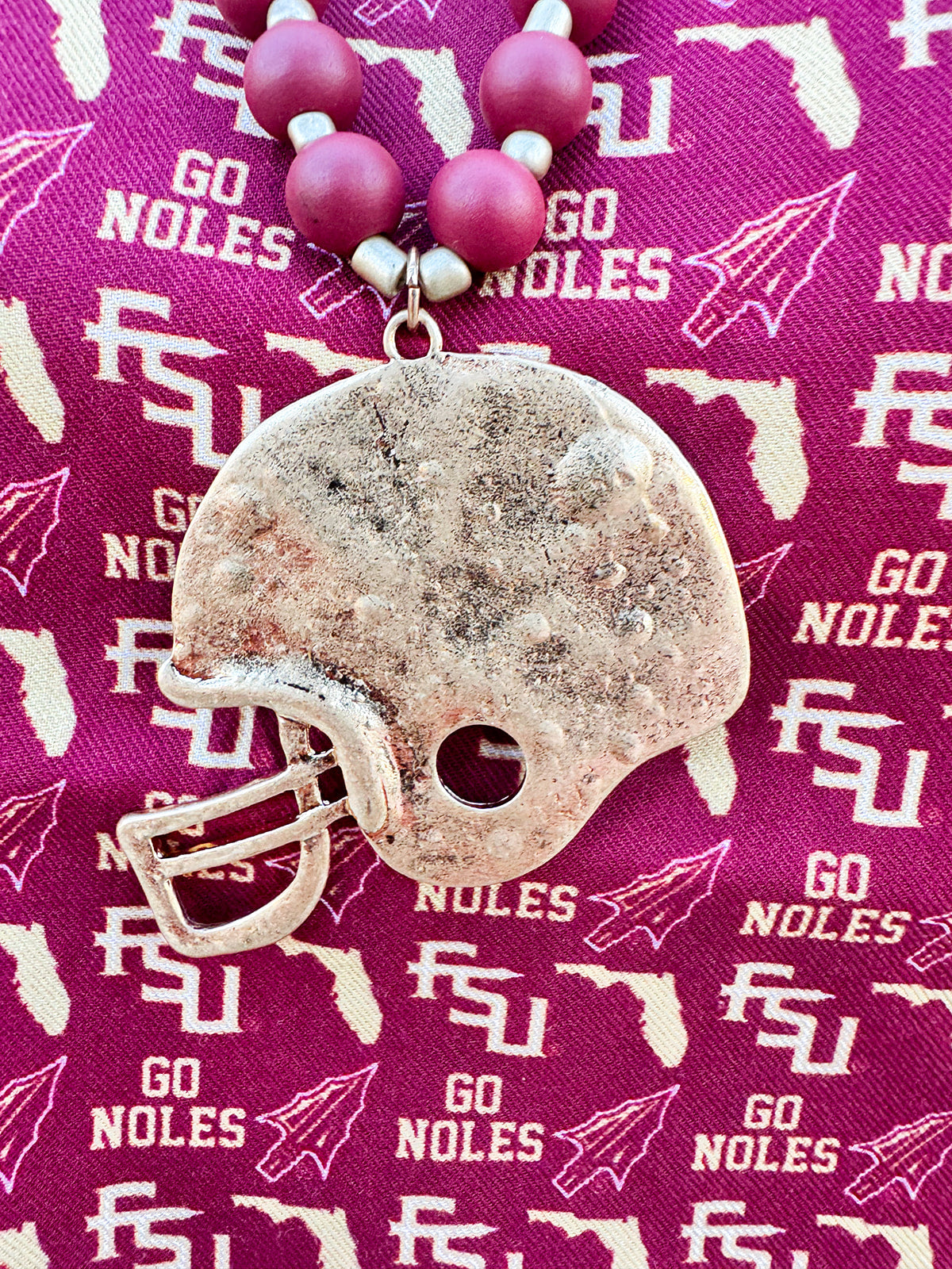 Garnet, black, and gold beaded necklace with a hammered gold football helmet pendant, styled for gameday or seasonal wear.