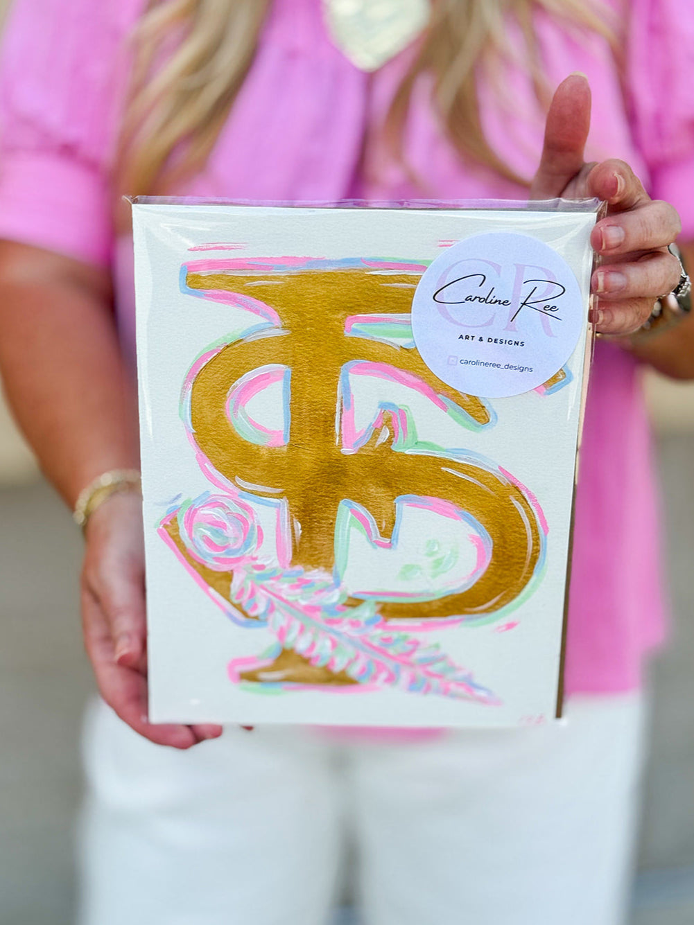 An 8"x10" hand-painted canvas featuring the Florida State FS logo with feather detail in vibrant pink, gold, and blue by Caroline Ree Designs.