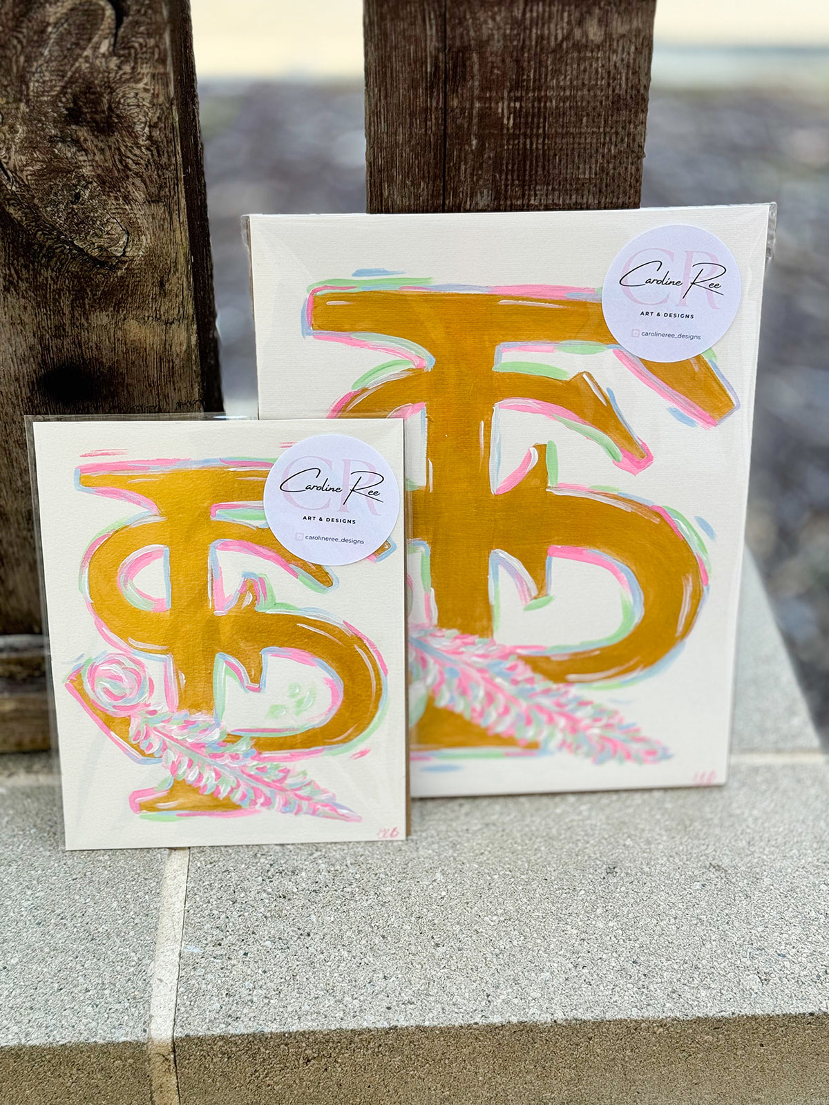 A brightly hand-painted 8"x 10" and 11"x14" canvas featuring the Florida State FS logo with a stylized feather in pink, gold, and blue tones by Caroline Ree Designs.