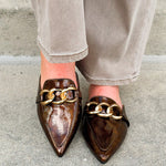 Bronze slip-on mules with glossy finish, gold chain detail, and pointed toe.