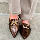 Bronze slip-on mules with glossy finish, gold chain detail, and pointed toe.