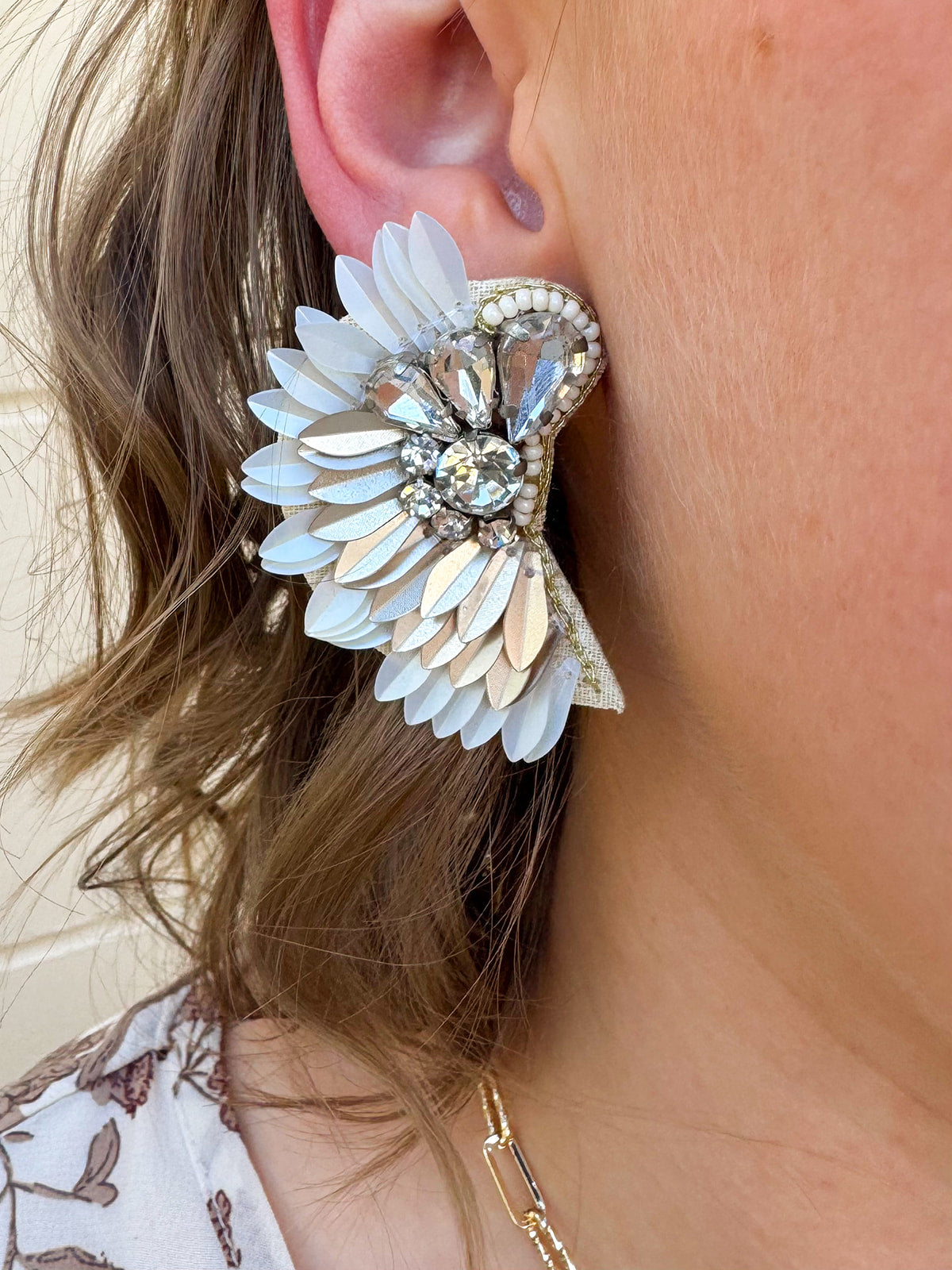 Gold and white feather-inspired earrings with a folded design and silver rhinestone cluster at the stud—lightweight with a bold, elegant look.