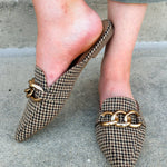 Houndstooth fabric mules with cream, brown, and black tones and a gold chain detail.