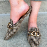 Houndstooth fabric mules with cream, brown, and black tones and a gold chain detail.