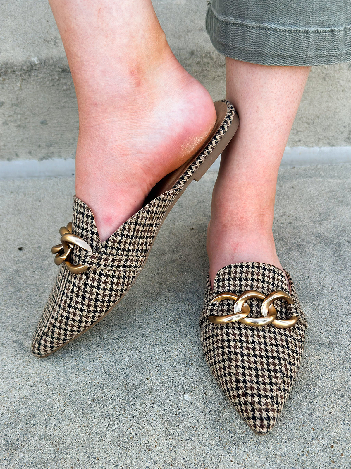 Houndstooth fabric mules with cream, brown, and black tones and a gold chain detail.