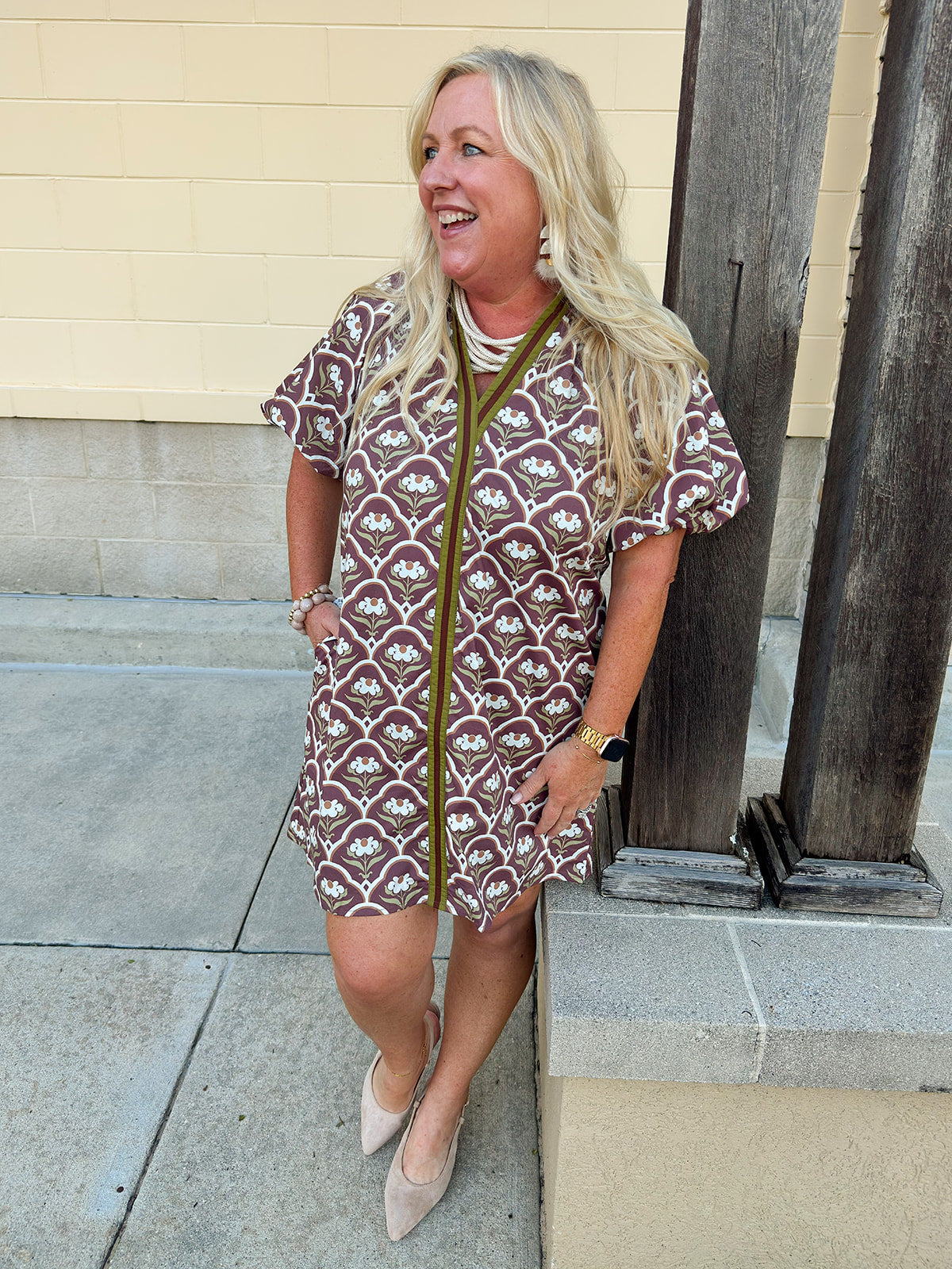 Brown and ivory botanical print mini dress with sage green binding, puff sleeves, ruffled V-neckline, and side pockets.