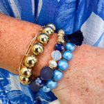Layered charm bracelet stack featuring blue and gold glass beads, gold accents, and a tassel pendant for a stylish, boho-inspired look.
