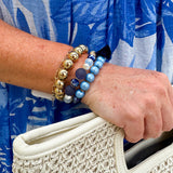 Layered charm bracelet stack featuring blue and gold glass beads, gold accents, and a tassel pendant for a stylish, boho-inspired look.