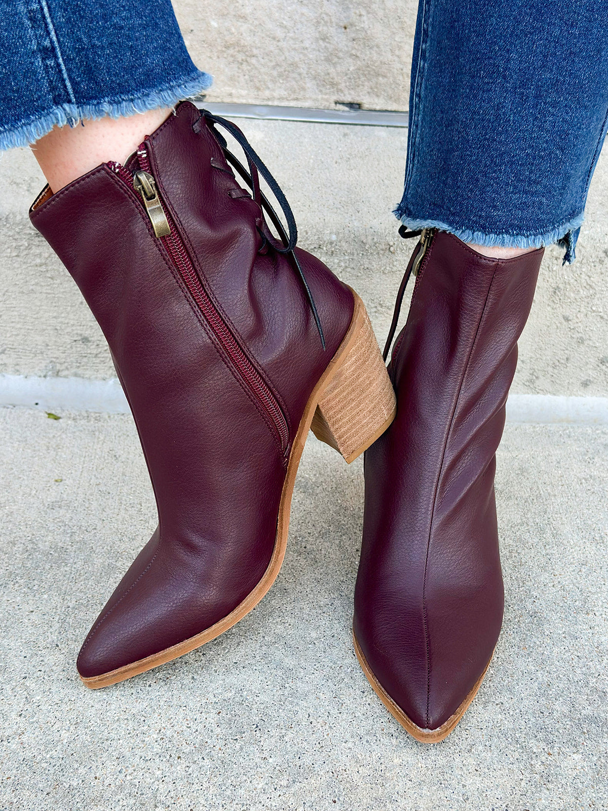 Garnet faux leather pointed toe ankle boot with stacked heel, inner side zipper, and lace-up back detail.
