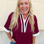 Burgundy boxy fit V-neck top with white contrast trim at neckline, collar, and sleeve cuffs.