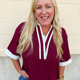 Burgundy boxy fit V-neck top with white contrast trim at neckline, collar, and sleeve cuffs.