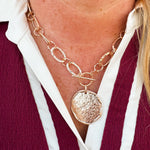 Short gold chainlink necklace with a toggle clasp and large hammered circle pendant.