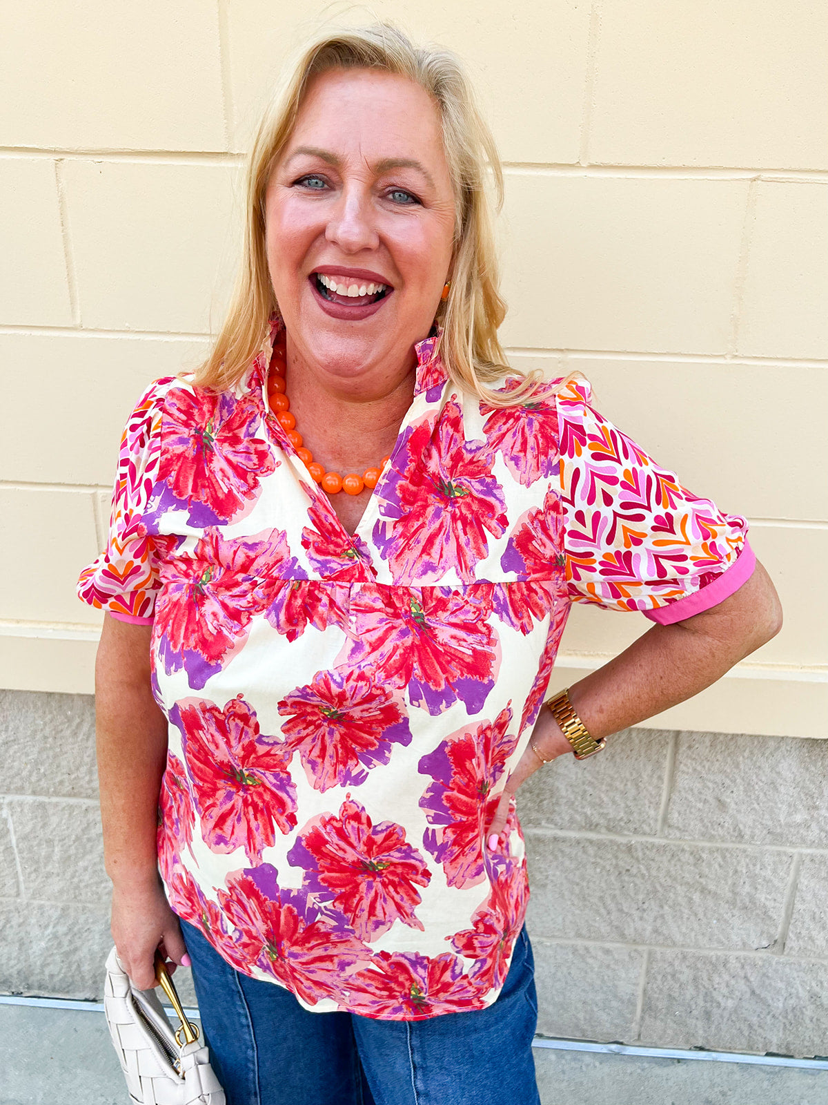 Cream blouse with pink, orange, and purple abstract detailing, ruffle collar, v-neckline, and contrast cuffed sleeves