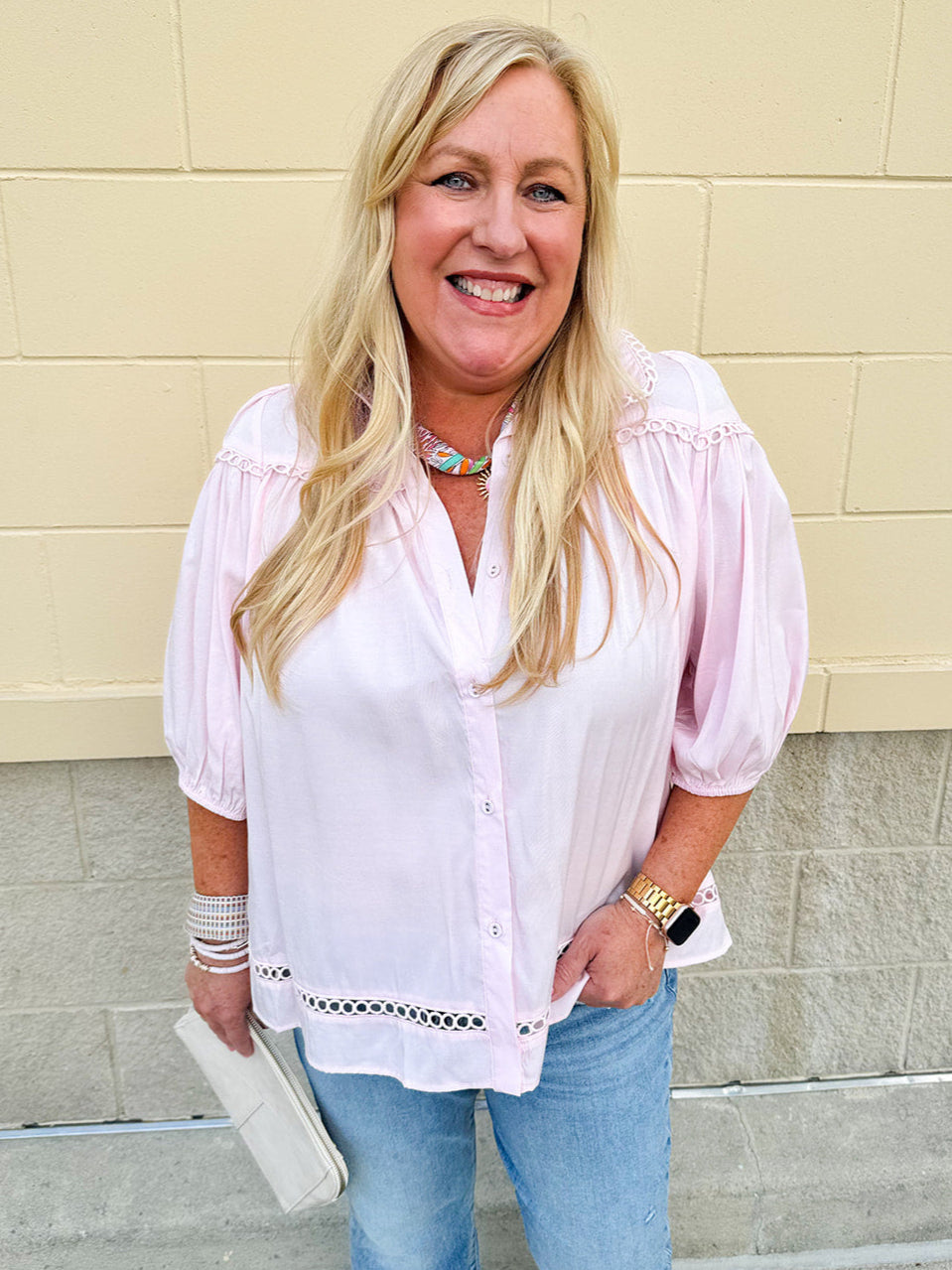 Solid pink button-down blouse with circular eyelet trim, ¾ sleeves, and pleated details, styled for a refined, feminine look.
