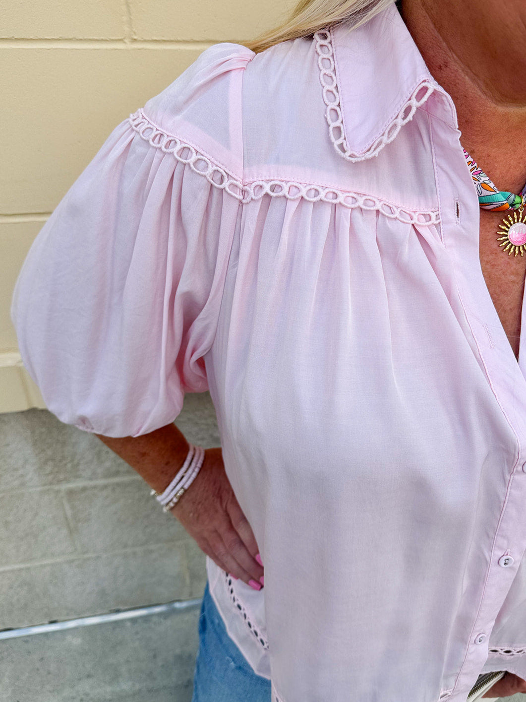 Solid pink button-down blouse with circular eyelet trim, ¾ sleeves, and pleated details, styled for a refined, feminine look.