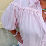 Solid pink button-down blouse with circular eyelet trim, ¾ sleeves, and pleated details, styled for a refined, feminine look.