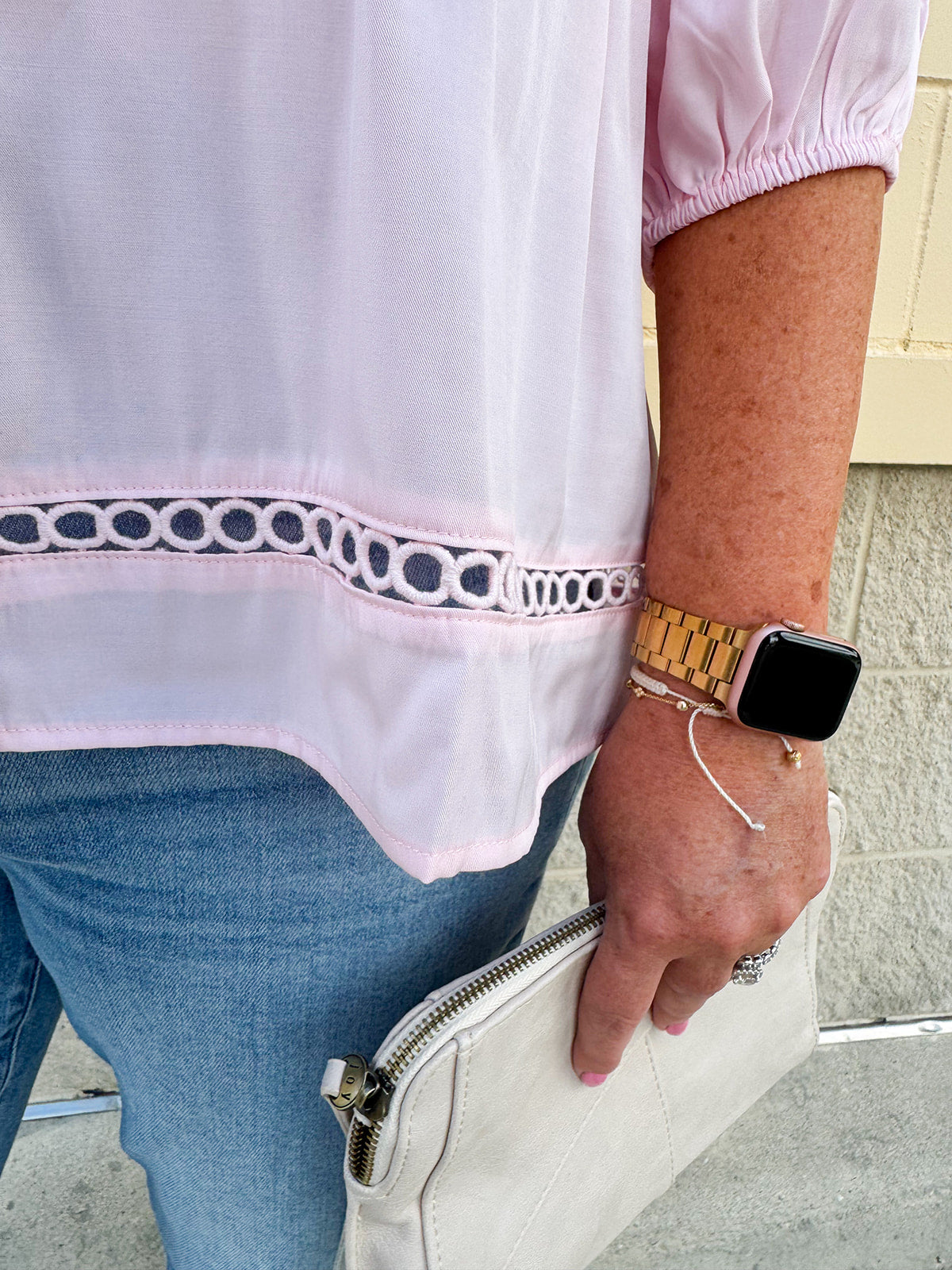 Solid pink button-down blouse with circular eyelet trim, ¾ sleeves, and pleated details, styled for a refined, feminine look.
