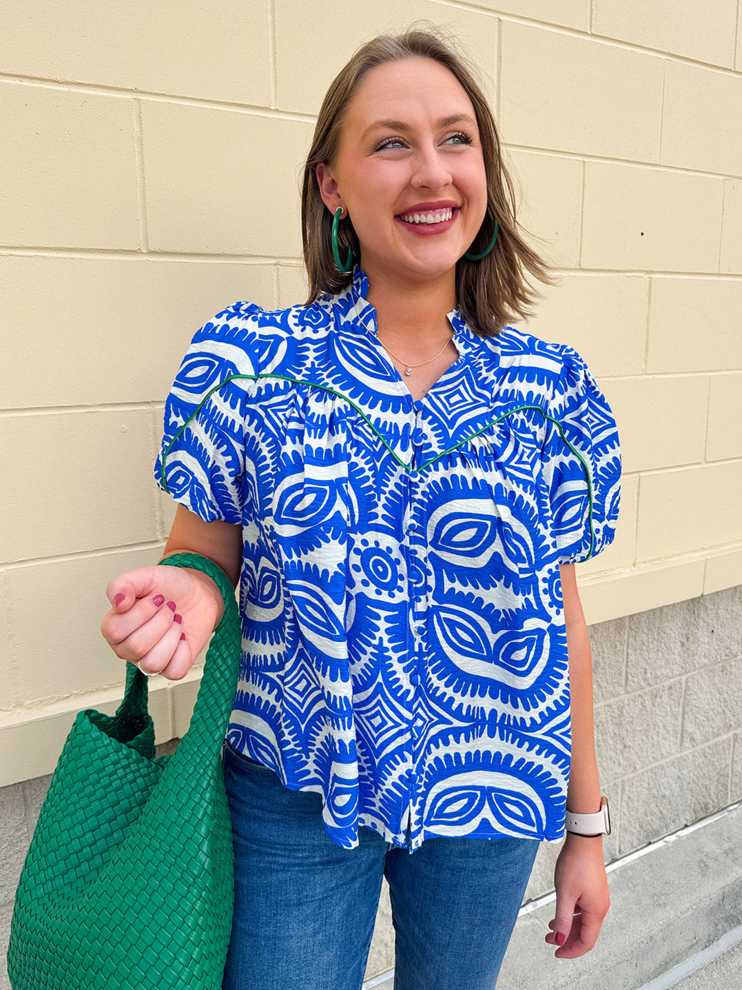 Blue and white patterned top with a ruffled collar, puff sleeves, and covered buttons, styled for a polished summer look.
